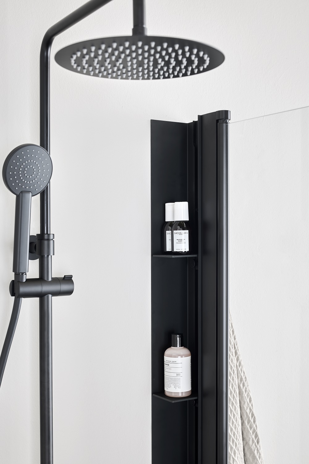 Mattsvart tak- och handdusch med inbyggd hylla och flaskor mot vit vägg