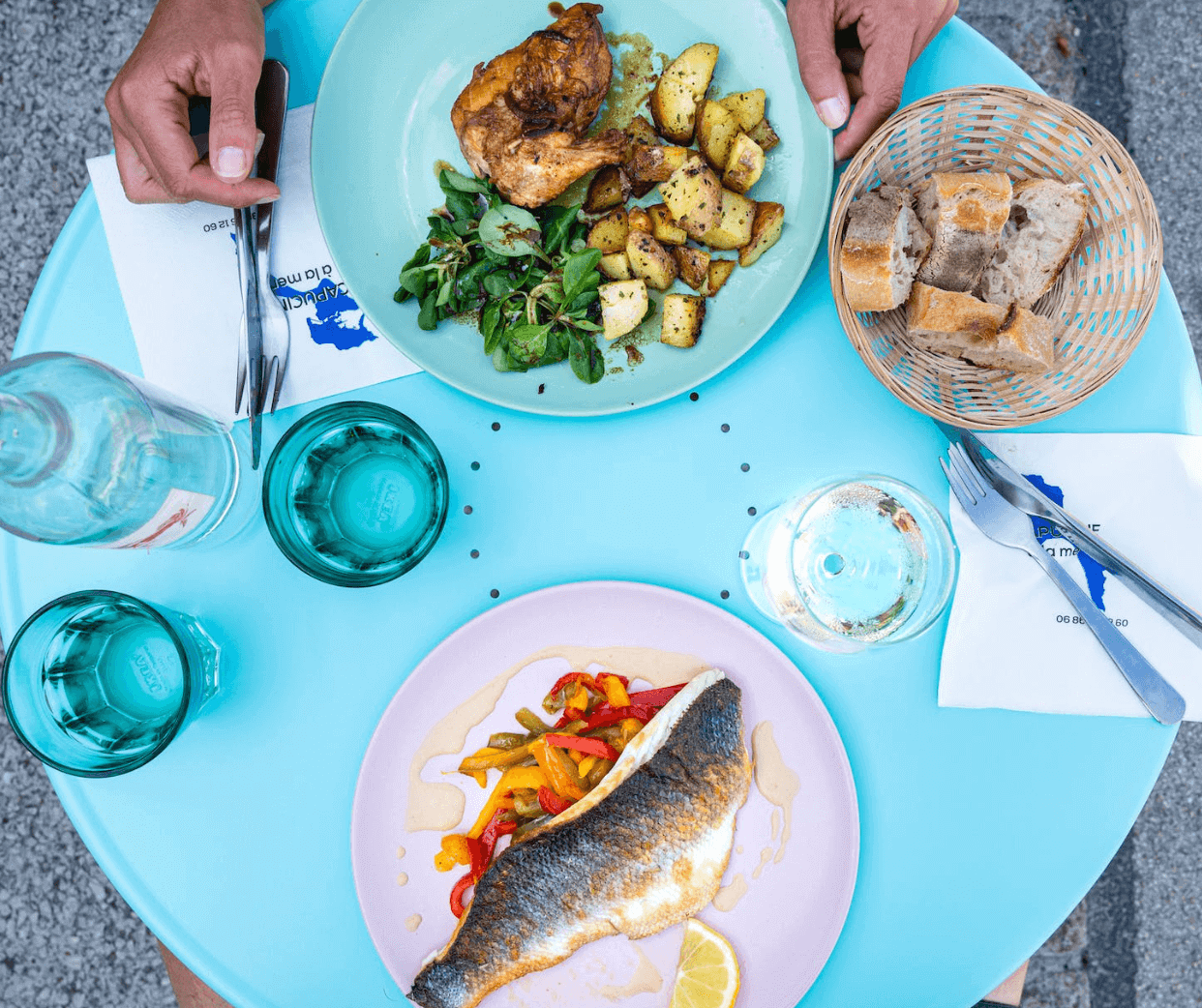 Blått cafébord med kyckling, rostade potatisar, sallad, stekt fisk med paprika, bröd och glas.