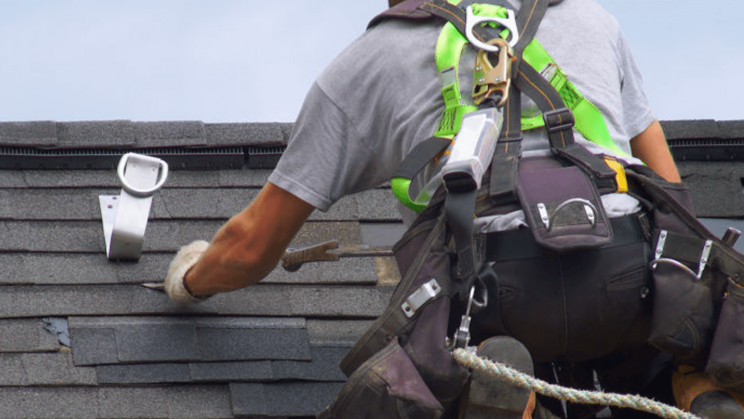 Takläggare med neongrön sele och verktygsbälte monterar grå takshingel.