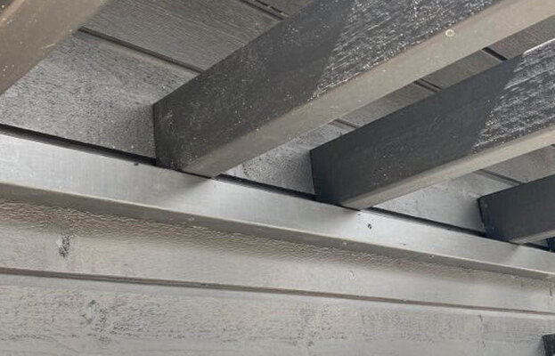 Närbild på mörkgråa träbjälkar och ljusgrå träpanel under uteplatsens däck.