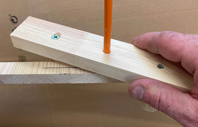 Hand håller två träbitar sammanfogade med en orange penna instucken i ett borrat hål