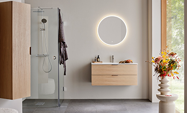 Dusch med glasvägg, flytande ljus trämöbel med rund LED-spegel, fönster och vas med blommor