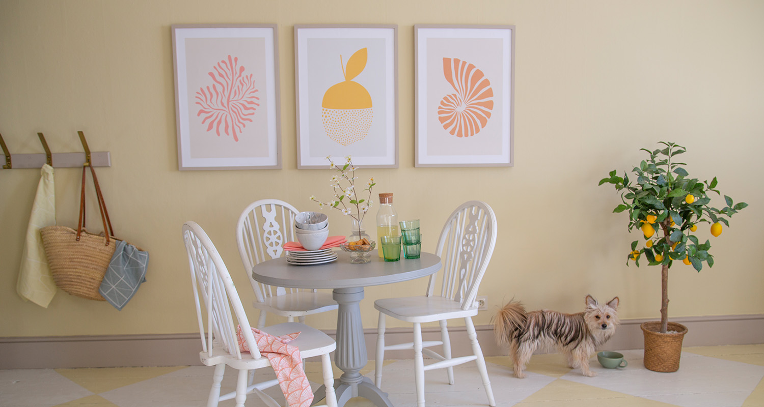 Rum med pastellgula väggar, vitt rundbord, minimalistiska tavlor, citronträd och liten hund