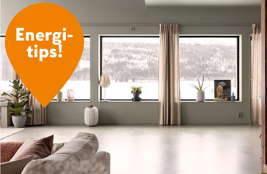 Vardagsrum med tre stora fönster mot snötäckta berg, beige gardiner och orange Energi-tips-bubbla