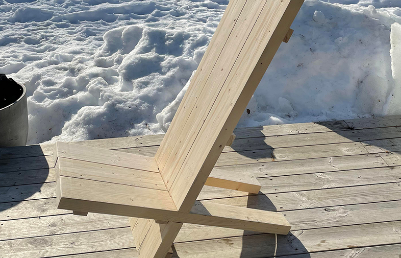 Ljus trästol på trädäck, snödrivor i bakgrunden i soligt vinterljus