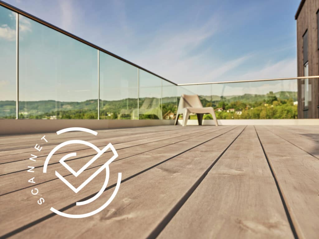 Solbelyst träaltan med glasräcke och ensam beige stol, grön utsikt under klarblå himmel.