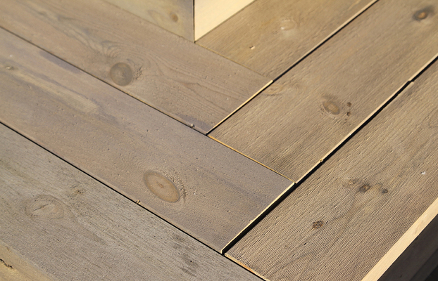 Närbild på grånat trävirke med synliga knutar och ådring vid ett hörn.