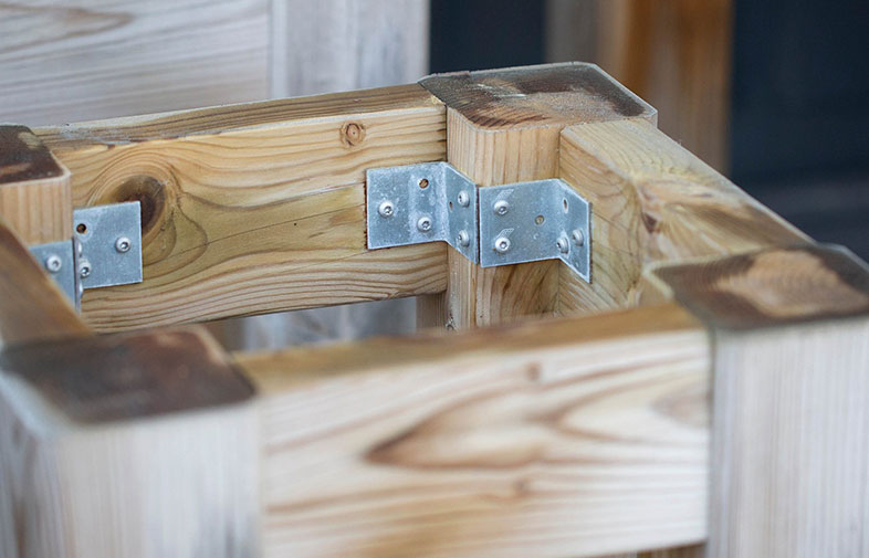 Närbild av ljus träställning med silverfärgade metallhörnbeslag.