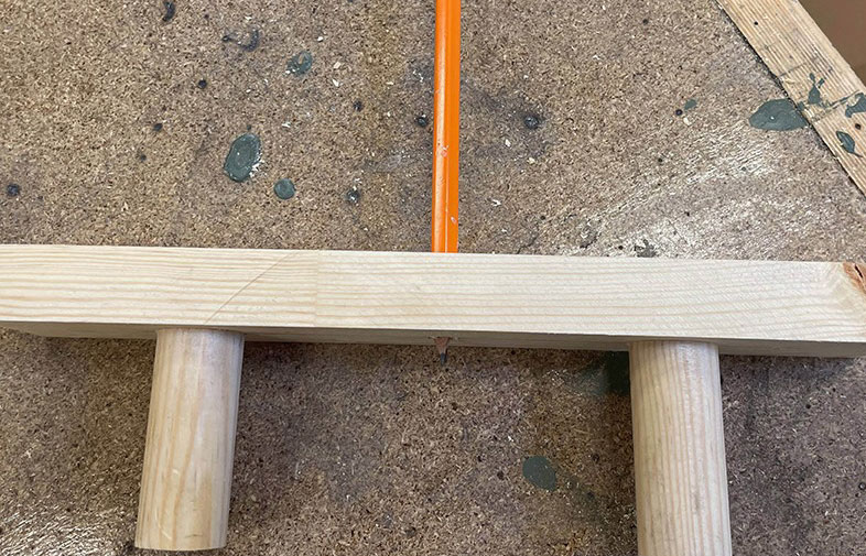 Ljus träregel med två träcylindrar som stöd och en orange kabel på brun arbetsbänk