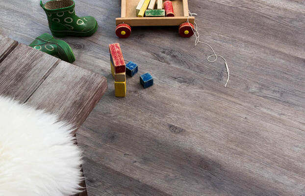 Grått vinylgolv med trävagn fylld av färgglada träklossar och gröna gummistövlar