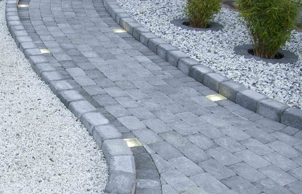 Grå, kurvad stenbelagd gång med infällda ljus, vitt grus och bambu.