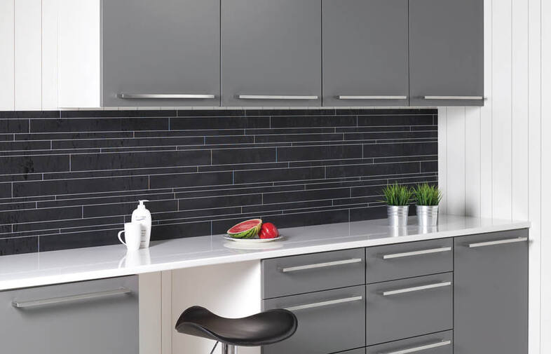 Köksbänk med grå skåp, svart kakel, vit bänkskiva, grön planta, diskmedel och melon.