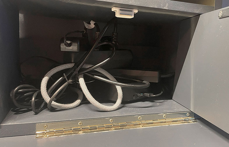 Inre av grått skåp med öppna dörrar, svart grenuttag och hoplindade svarta och grå kablar.