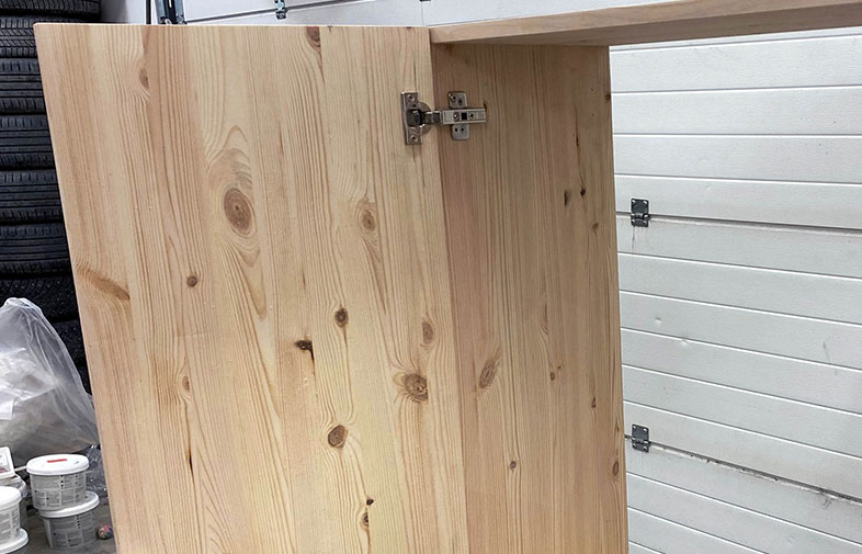 Ljus obehandlad träskiva med kvistar och gångjärn i garage med däck och vit port