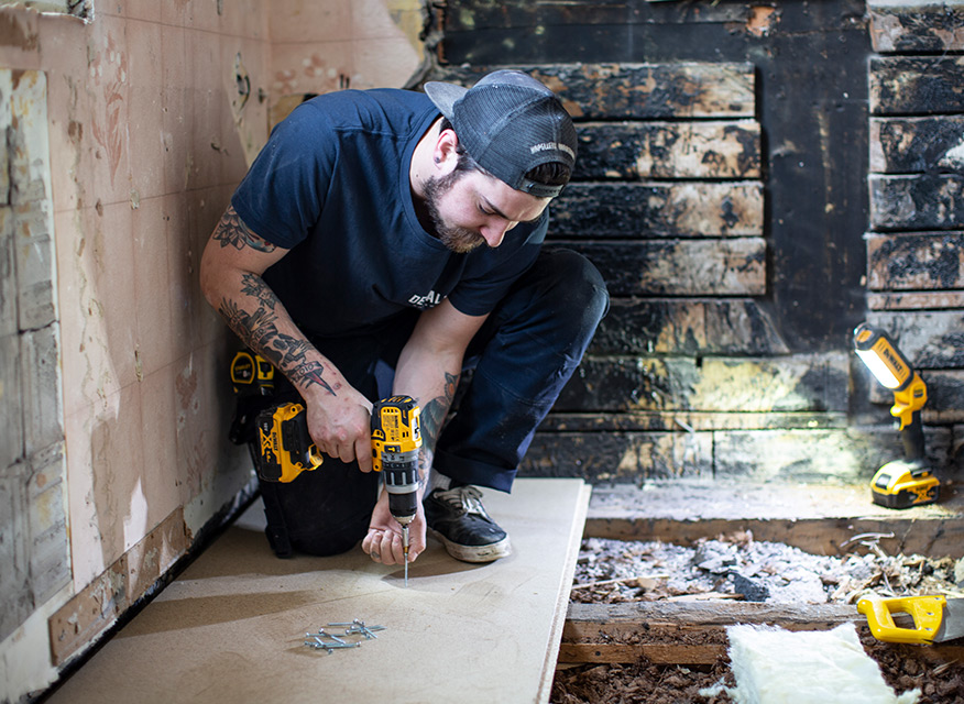 Lägga golv i badrum. Med skruvdragare dras golvet fast i reglarna