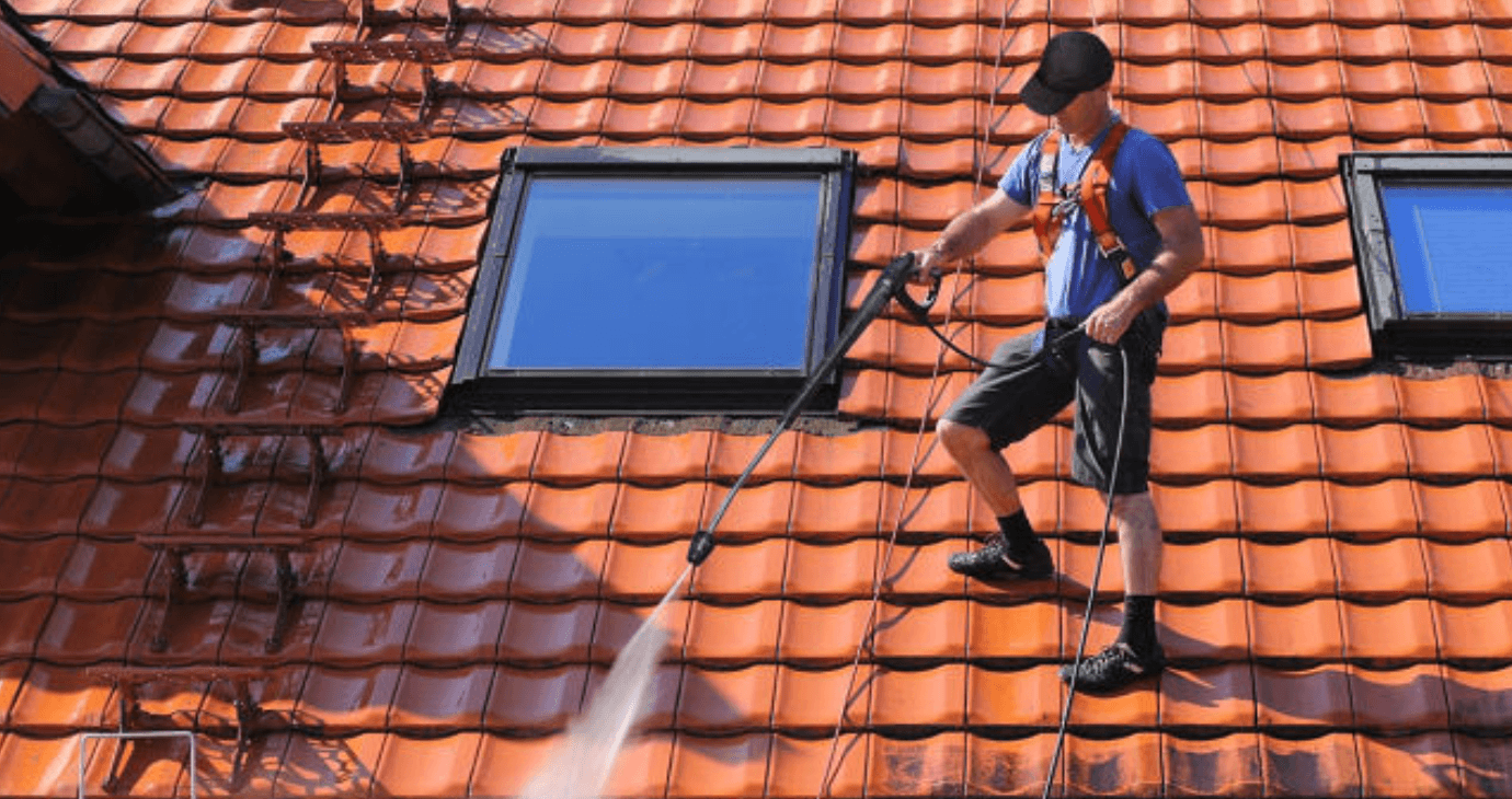 Person i säkerhetssele högtryckstvättar rött tegeltak med två takfönster.