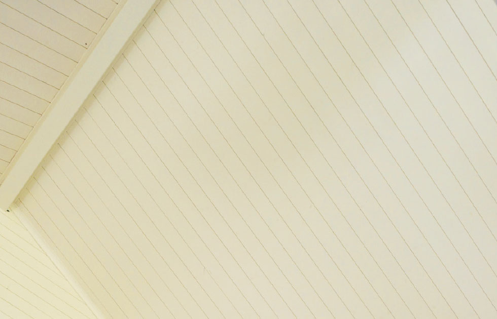 Inomhus snedtak i krämfärgade träpaneler med synlig bärande balk