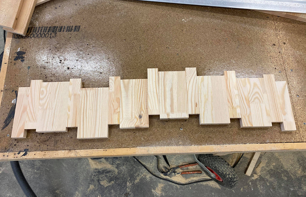 Ljus träkonstruktion i pusselmönster på verkstadsbänk med sågspån och verktyg