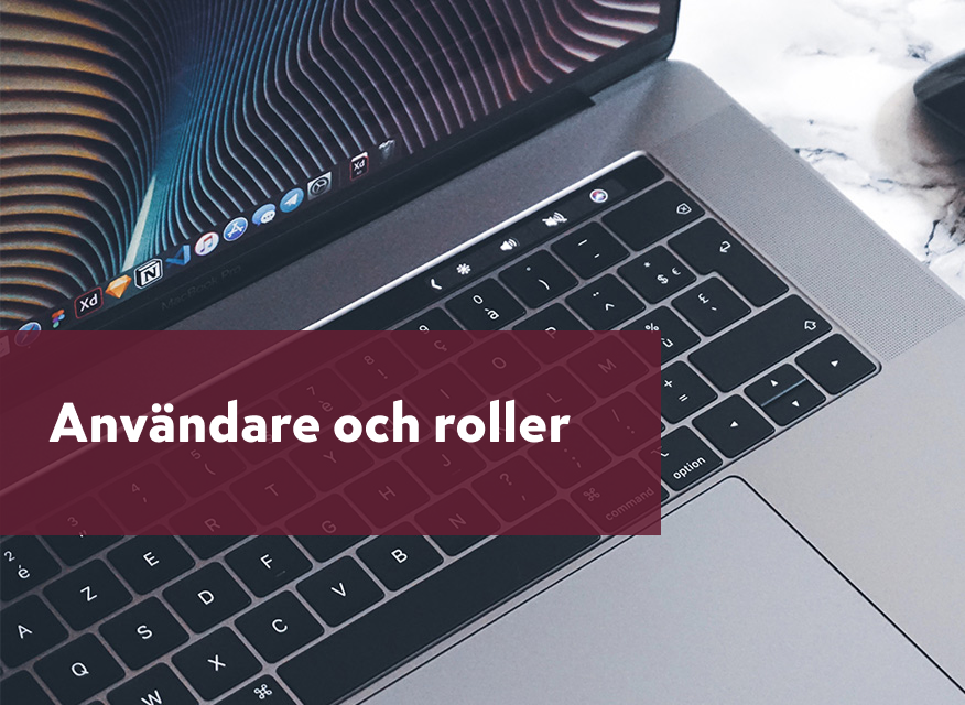 närbild på en öppen laptop i metall, med fokus på tangentbordet och nedre delen av skärmen. Ovanpå ligger en vinröd transparent ruta med texten “Användare och roller”.