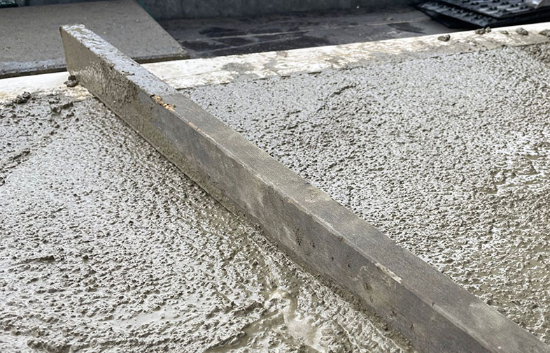 Närbild av träregel som jämnar ut nygjuten grå betong på golvyta under arbete