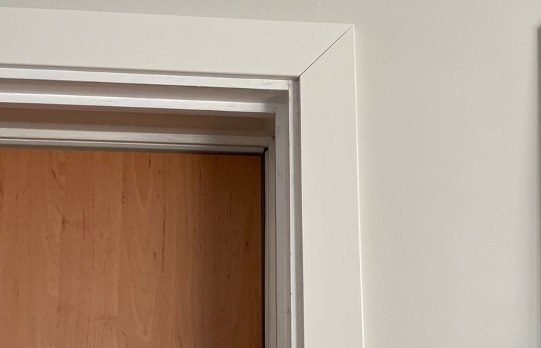 Ljusbrun innerdörr med vit karm och vägg, metallskena synlig ovan dörren.
