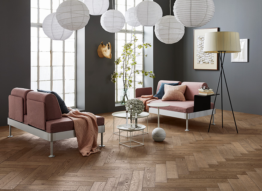 Ljust vardagsrum med grå vägg, rosa soffor, vita papperslampor, stora industrifönster och träparkett