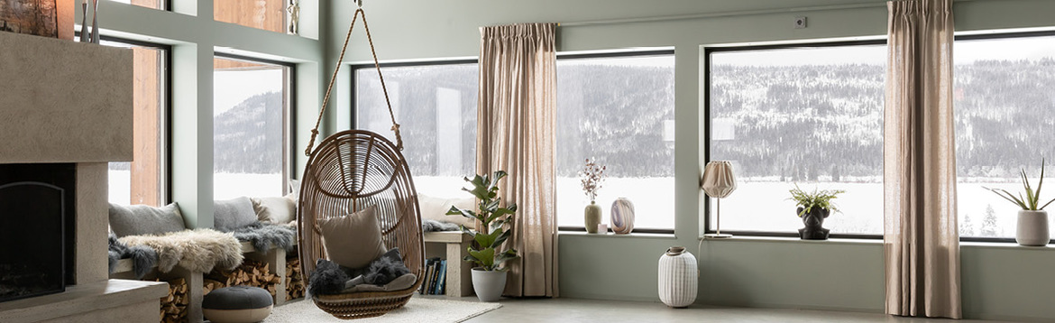Ljust vardagsrum med gröna väggar, höga fönster mot snölandskap, rottinggunga och eldstad