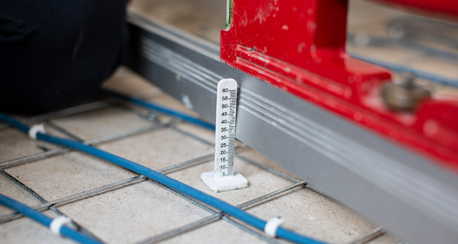 Vit mätskala vid grå räls och rött verktygsstöd på golv med blå rör och armeringsnät