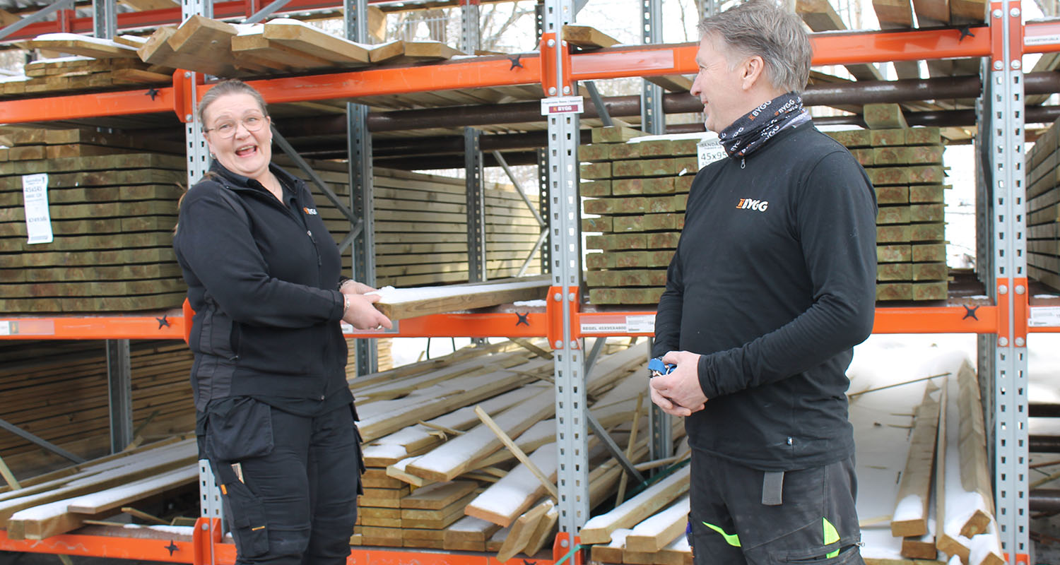 Två personer i svart arbetsklädsel vid orange ställning med snötäckta träplankor utomhus