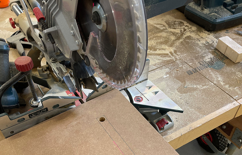 Kapsåg med silverblad och röda vred på dammig arbetsbänk med brunt skivmaterial och sågslinje.