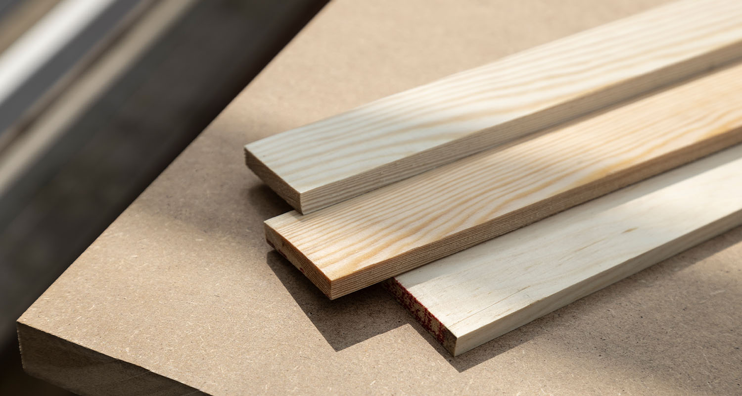 Tre ljusa träplankor med synliga årsringar på beige bordsskiva i solljus.