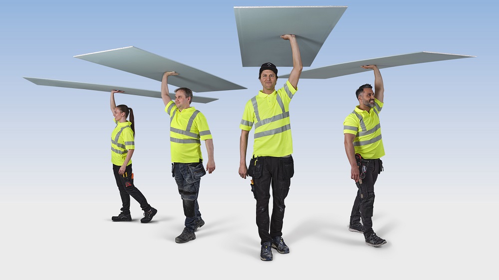 Fyra byggarbetare i gula reflextröjor bär stora skivor över huvudet mot ljus bakgrund.