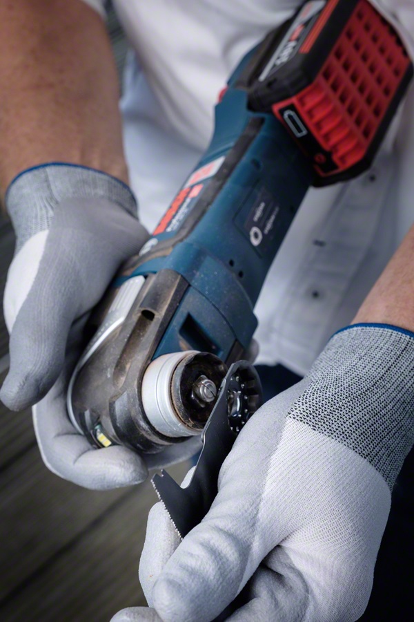 Gråhandskade händer monterar blankt sågblad på blå-svart batteridriven multiverktyg.