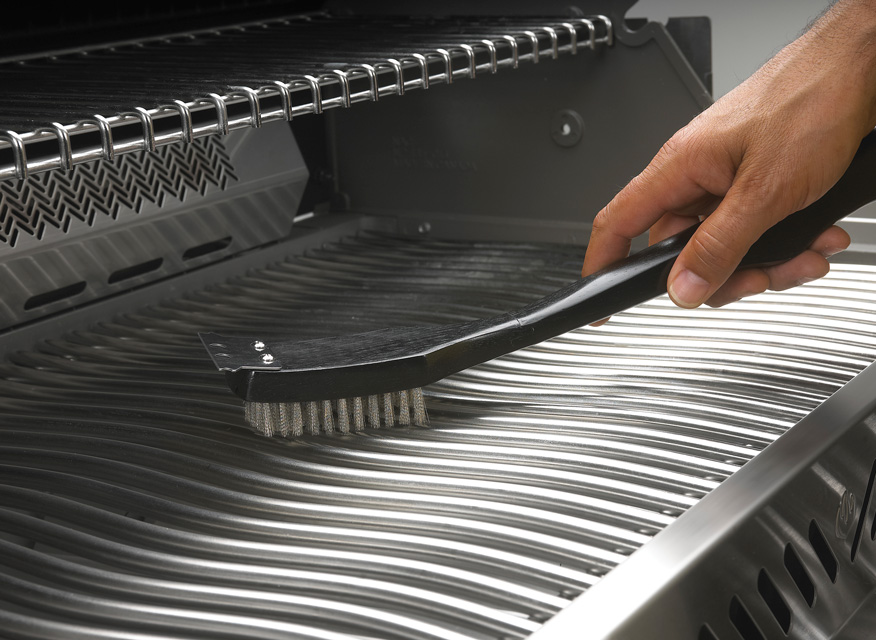 Hand som rengör blankt rostfritt stålgrillgaller med svart borste