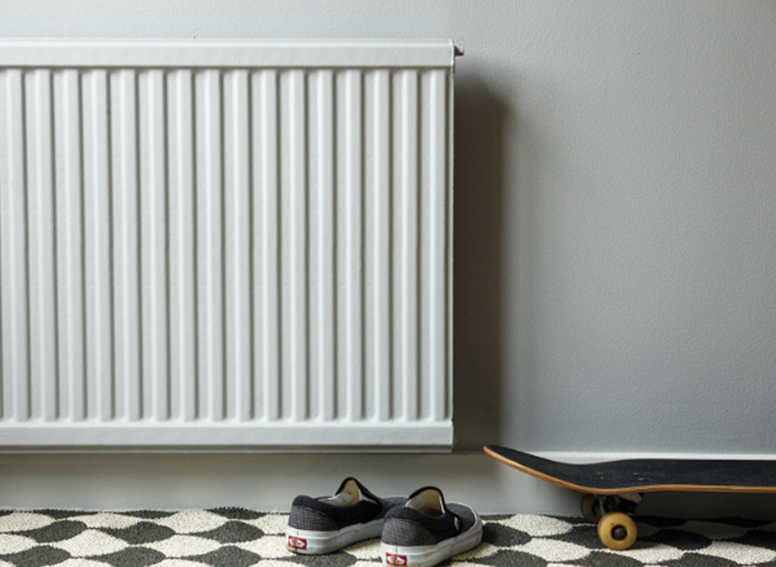 Vit element på ljusgrå vägg, mönstrad matta med svarta sneakers och skateboard på golvet.