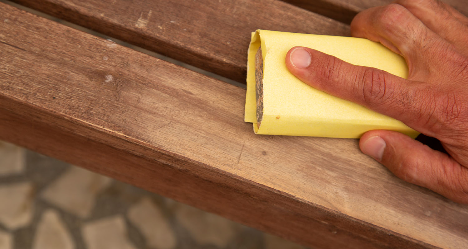 Hand slipar brun träbänk med gul slipkloss utomhus på stenbelagd yta