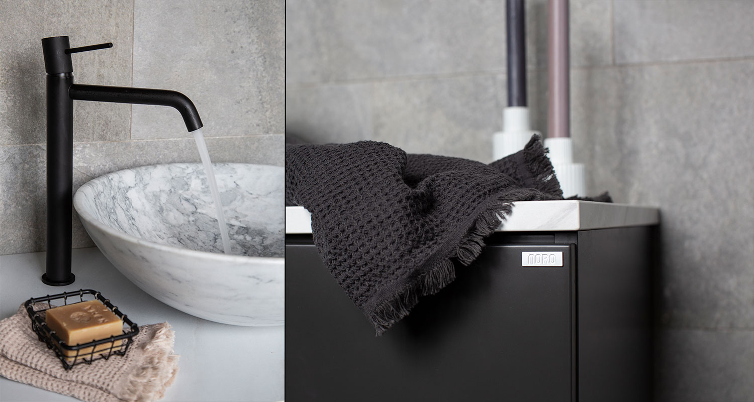 Vit marmorhandfat med rinnande svart kran, beige tvättlapp med tvål, svart skåp med mörk handduk