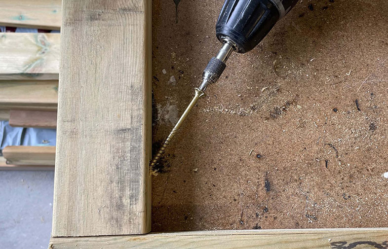 Svart borrmaskin driver guldfärgad skruv i ljusgrönt trä på arbetsbänk