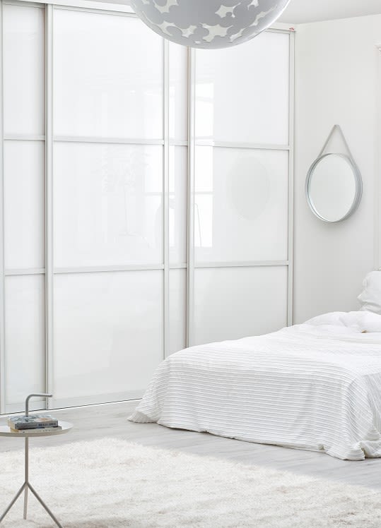 Ljust vitt sovrum med vitrandig säng, stjärnhänglampa, rund spegel och glasbord.