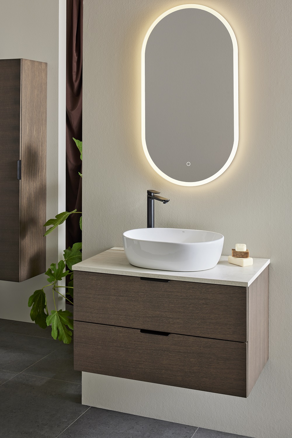 Modern badrumskommod i mörkt trä med vit ovalt handfat, svart kran och belyst spegel