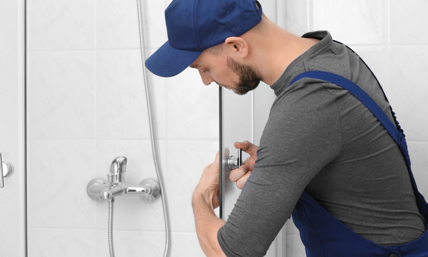 Rörmokare monterar glasduschdörr i vitt kaklat badrum med kromad duschblandare