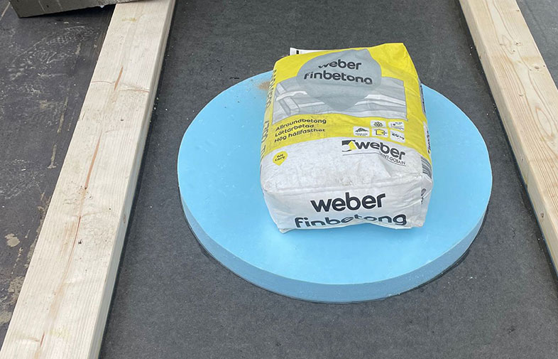 Vit-gul säck Weber finbetong på blå rund isoleringsskiva mellan två träreglar.