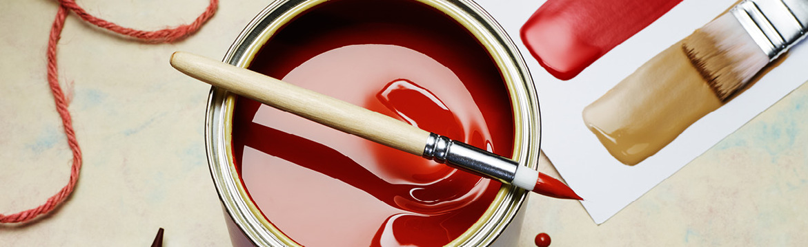 Närbild på öppen färgburk med röd färg, pensel, garnsnutt och färgprover i rött/beige