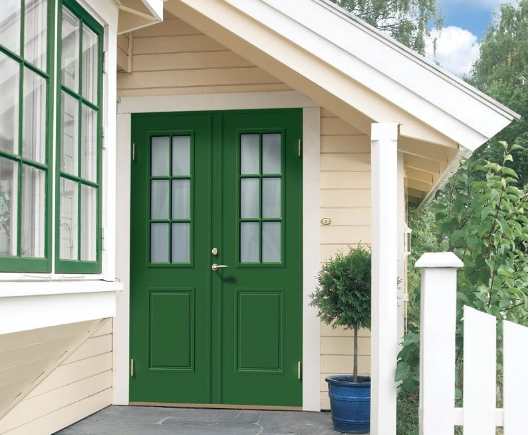 Entré på ljust trähus med vit veranda, mörkgrön glaspardörr och krukad buske