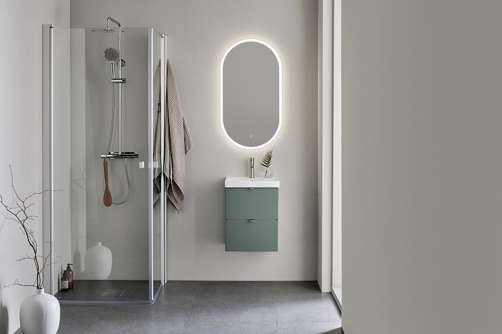 Modernt grått badrum med glasdusch, hängande handduk, grönt skåp under oval spegel med belysning.
