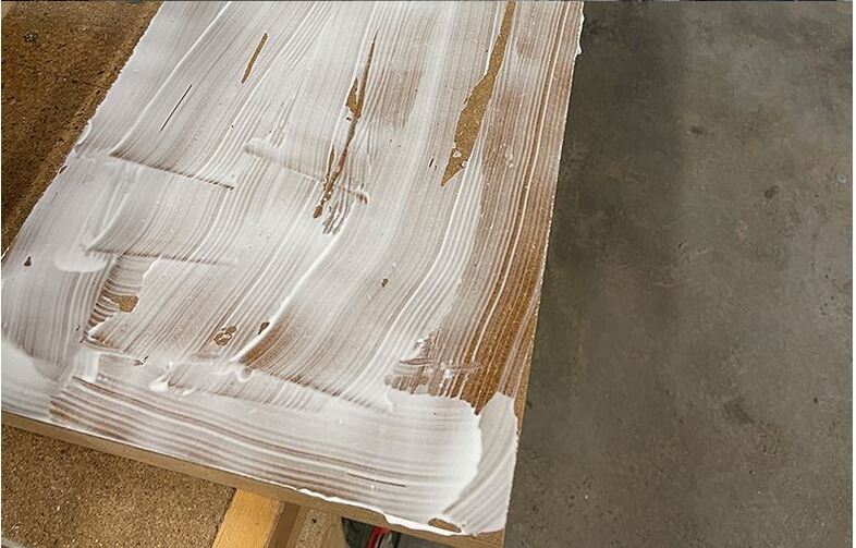 Delvis vitmålad träskiva på ställning i verkstad med betonggolv