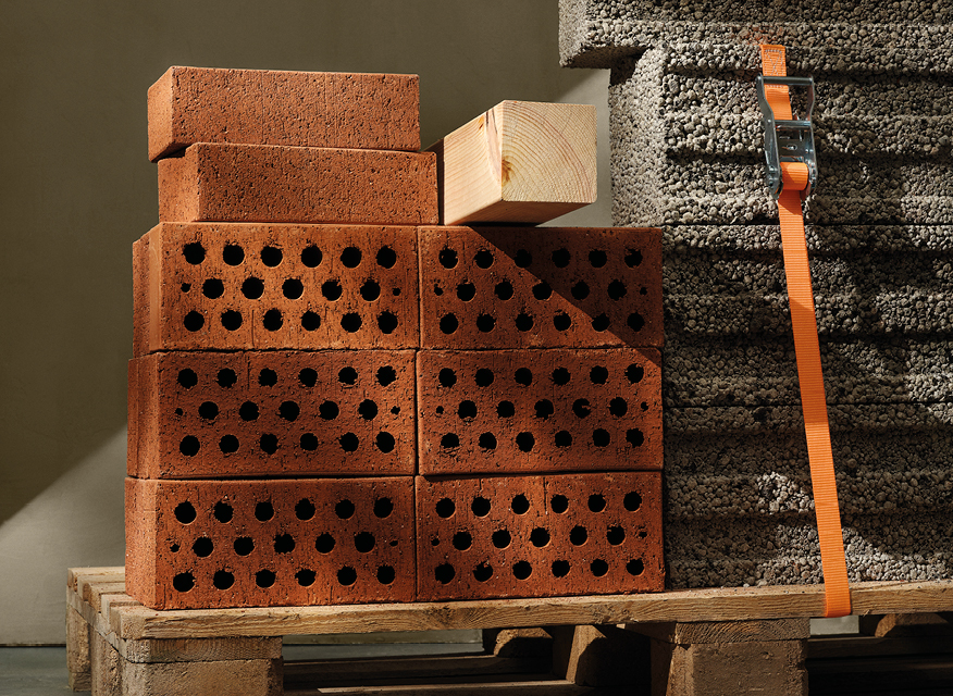 Röda håltegel på träpall bredvid grå isoleringsblock fastspända med orange band