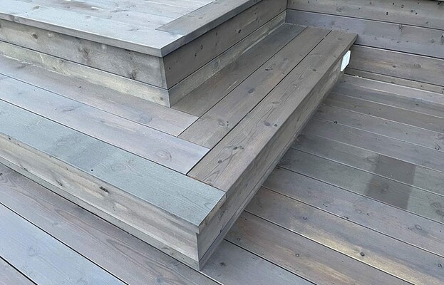 Grått uteplatsdäck i trä med breda hörntrappsteg av liggande plankor.