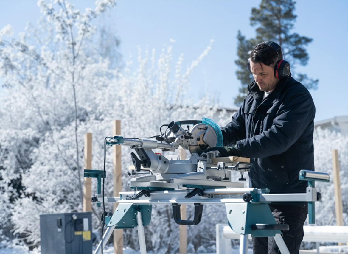 Man i grå t-shirt borrar trallbräda med batteridriven skruvdragare på solig uteplats.