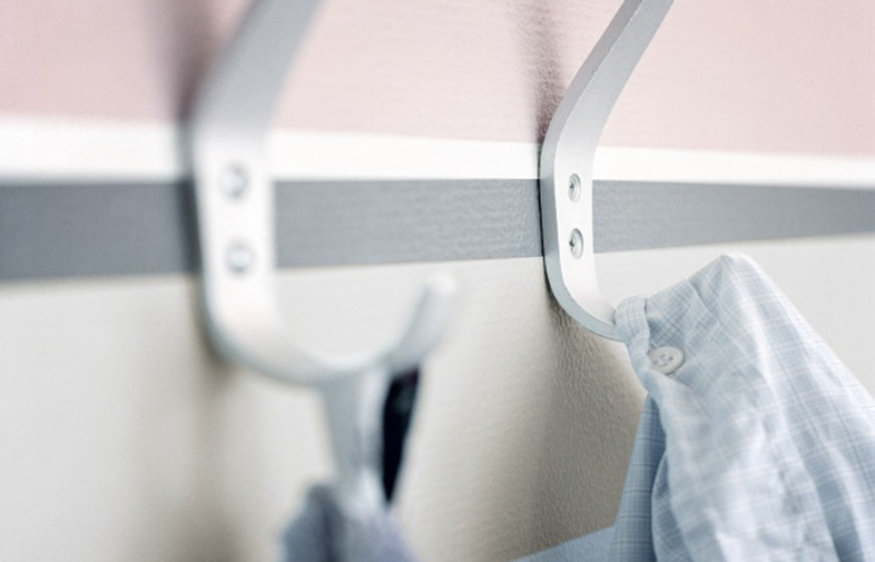 Vita metallkrokar på tvåfärgad vägg (rosa, vitt med grå rand) bär ljusblå rutig skjorta